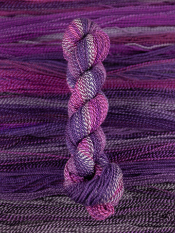 Skein of multicolored handspun looking wool yarn in the colors white dark purple light purple pink dark grey