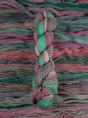 Skein of multicolored handspun looking wool yarn in the colors green pink grey teal brown