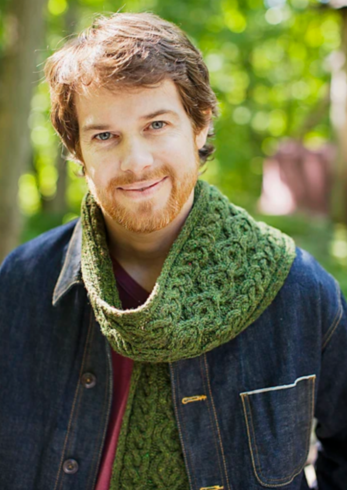 A man wearing a knitted, cabled scarf