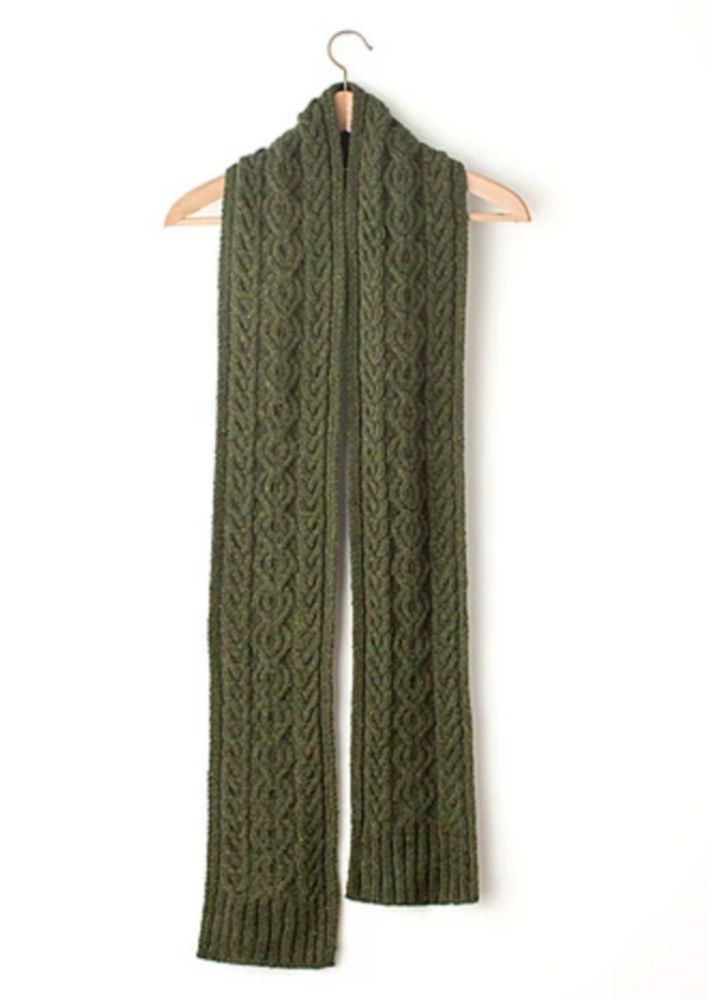 A knitted, cabled scarf hanging against a white background