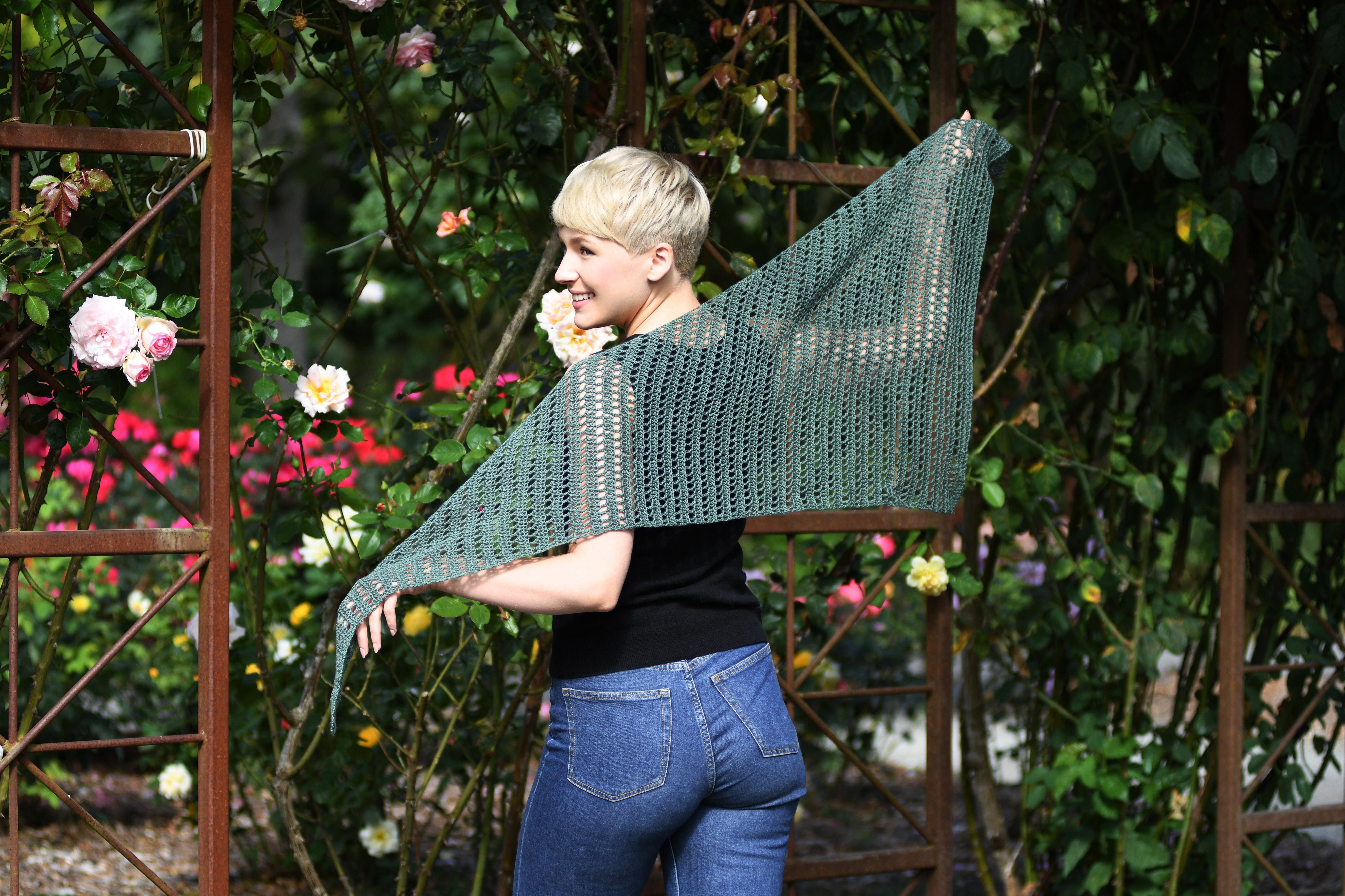 Woman with back to the camera showing off the Nardis Shawl in a rose garden