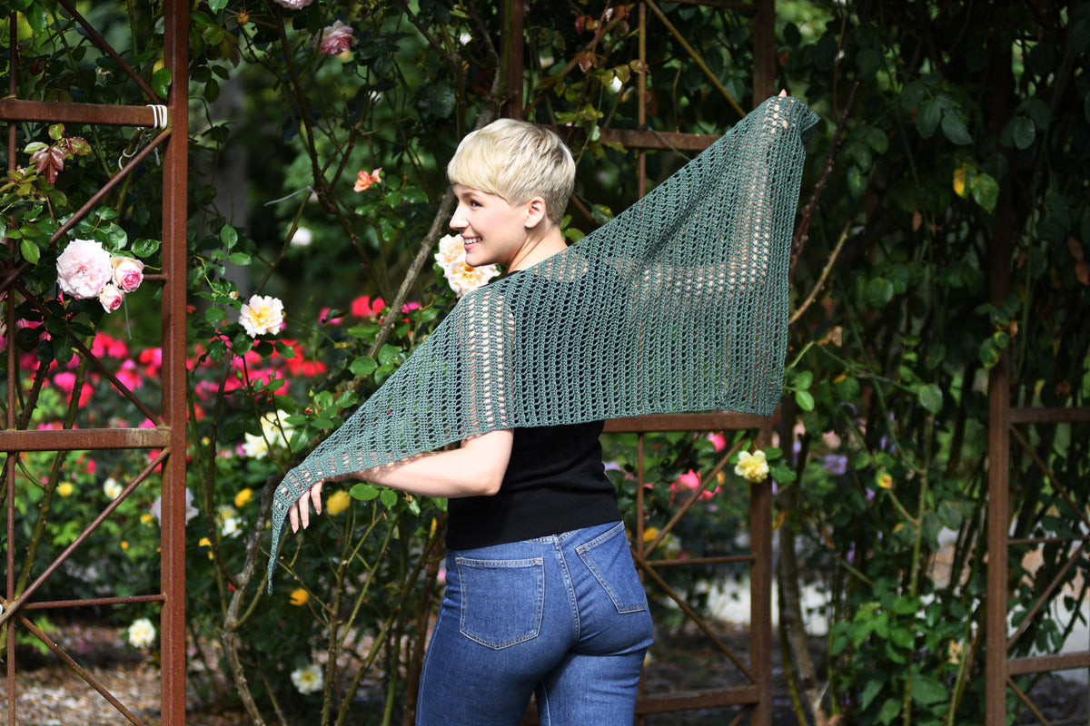 Woman with back to the camera showing off the Nardis Shawl in a rose garden