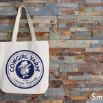 White tote bag with blue logo against a stone wall background