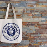 White tote bag with blue logo against a stone wall background