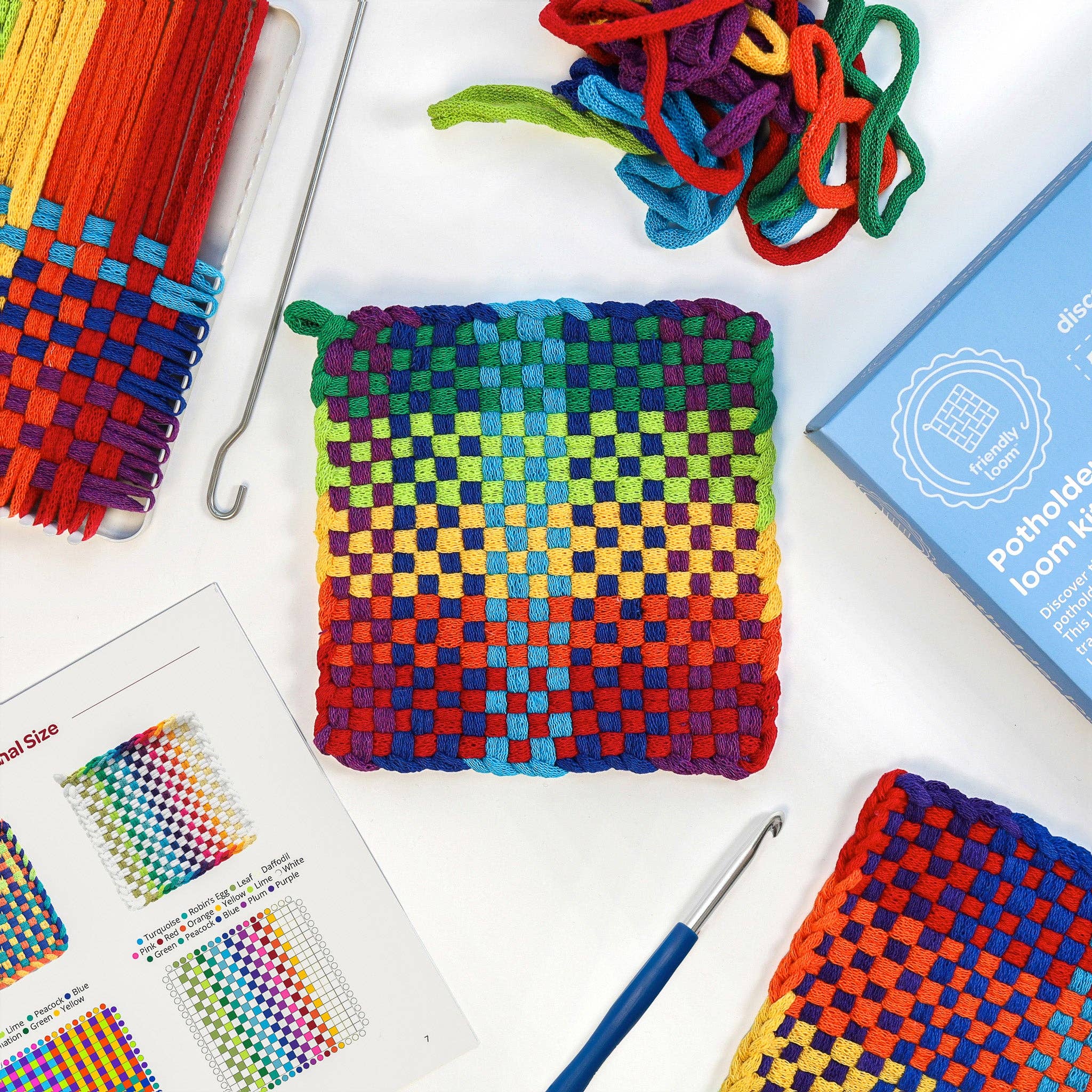 Colorful woven potholder with loom kit components on a white background