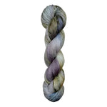 A skein of hand-dyed fingering/sock yarn color white grey tan blue purple black speckles