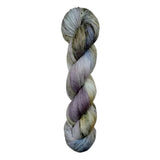 A skein of hand-dyed fingering/sock yarn color white grey tan blue purple black speckles
