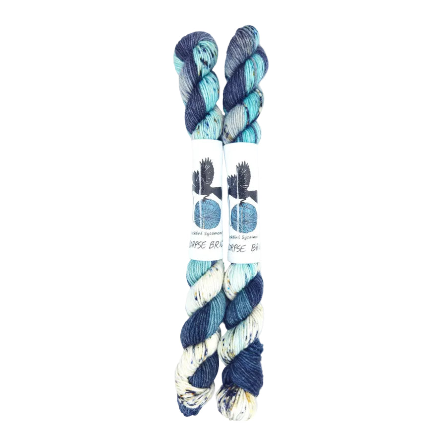 Blackbird Sycamore Fingering Mini Skein color variegated dark blue with streaks of light blue and white, and flecks of yellow and black