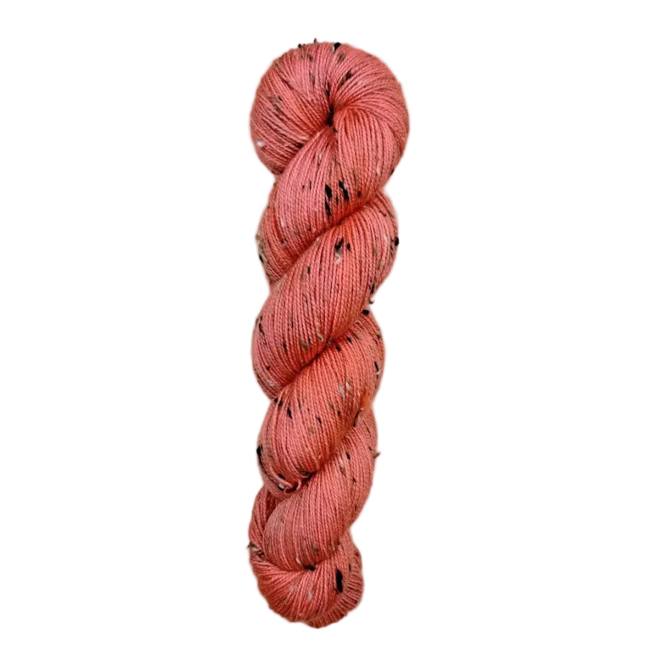 Peach-colored yarn skein with black speckles on a white background