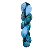 A skein of hand-dyed fingering/sock yarn color blue green black speckles