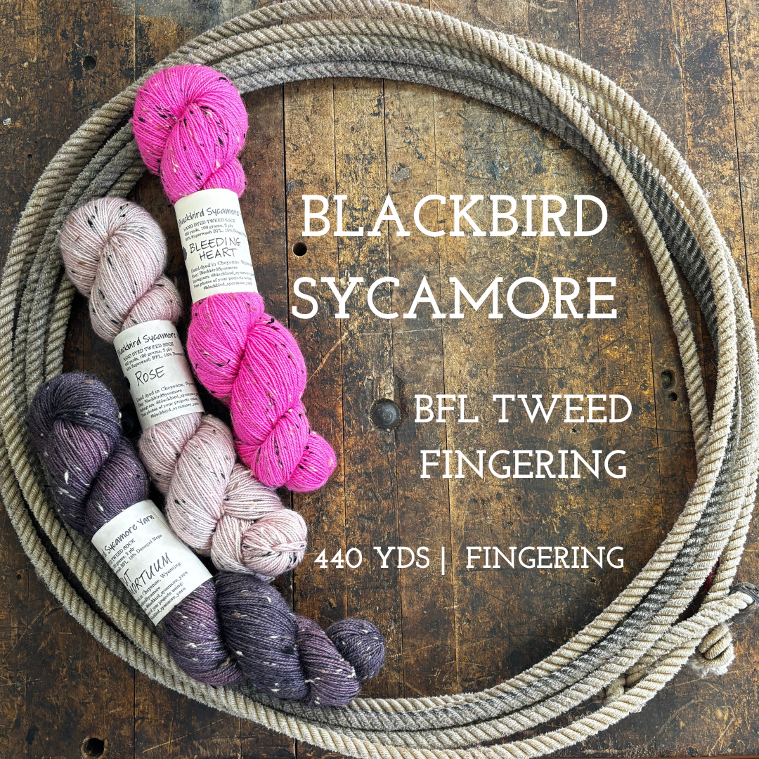 Skeins of hand dyed BFL Tweed Yarn color pink dusty rose purple on a wooden surface