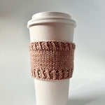 A Base Doodle Cup Cozy knit in light brown yarn on a disposable cup