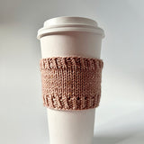 A Base Doodle Cup Cozy knit in light brown yarn on a disposable cup