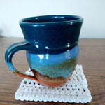 A mug on top of the white begin to crochet coaster