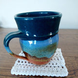 A mug on top of the white begin to crochet coaster