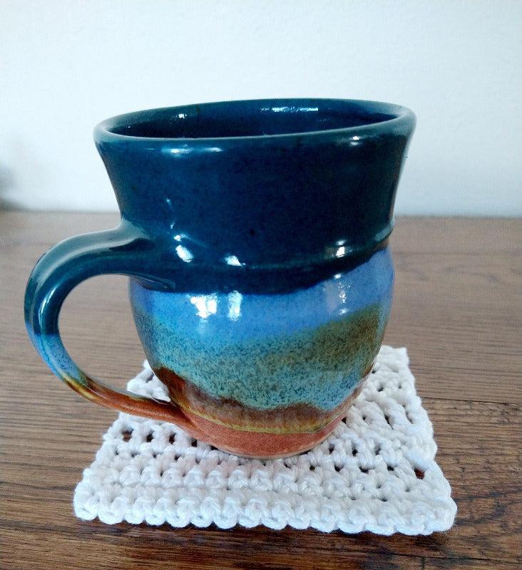 A mug on top of the white begin to crochet coaster