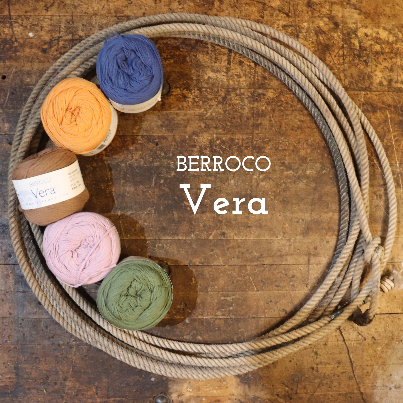 A coiled beige rope or cord arranged in a circle on a rustic wooden surface, with five balls of yarn in brown, orange, blue, pink, and green placed along the upper left curve. White text in the center reads 'BERROCO Vera'.
