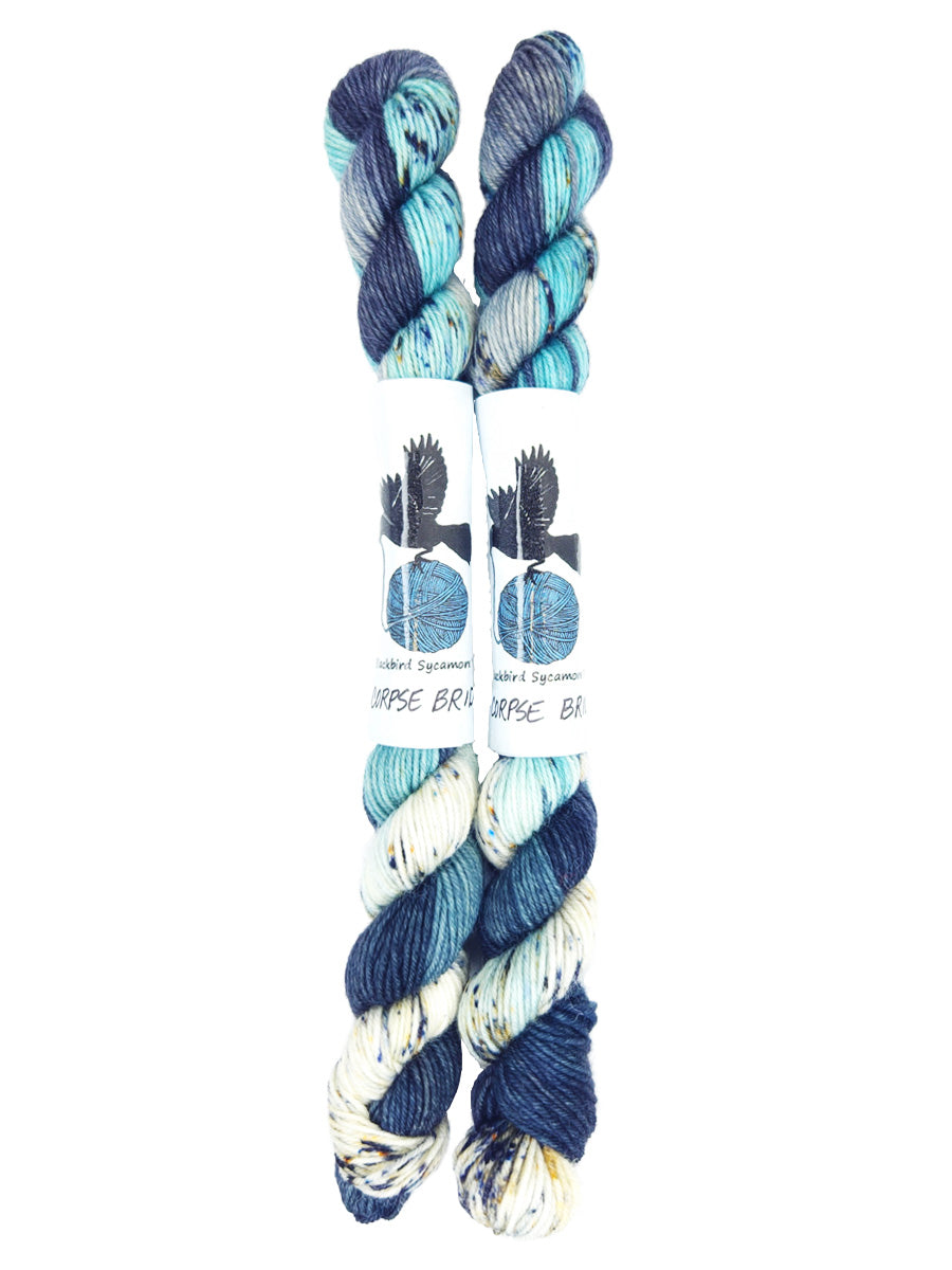 Blackbird Sycamore Fingering Mini Skein color variegated dark blue with streaks of light blue and white, and flecks of yellow and black