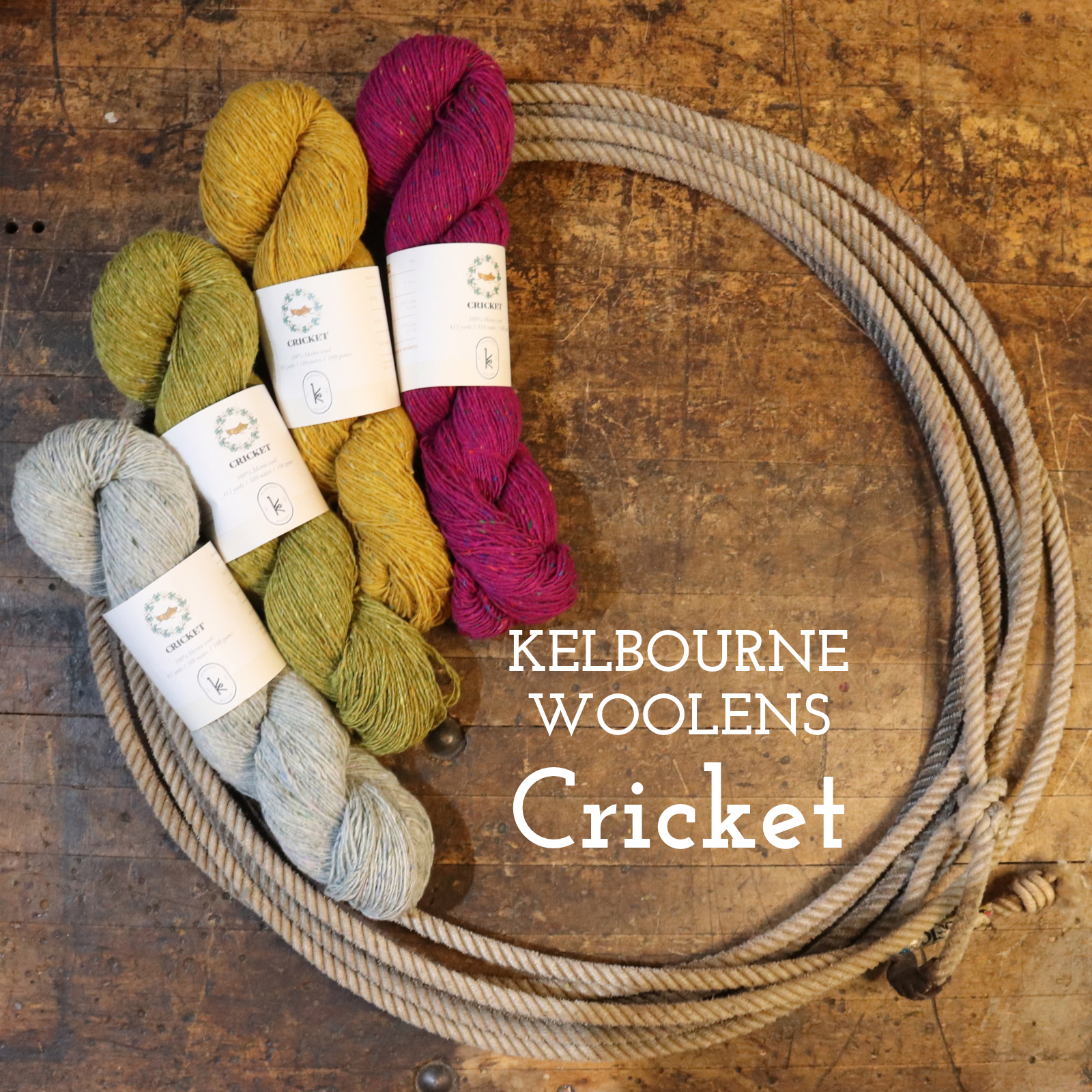 Four skeins of wool yarn in different colors arranged next to a coiled piece of natural fiber rope on a rustic wooden surface. The yarn colors are light gray, mustard yellow, olive green, and magenta.