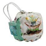 A small fabric drawstring pouch with white elastic loops and a mint green mesh side pocket, printed with a watercolor wheelbarrow and flowers on a white background.