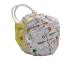 A small fabric pouch with a white background and a print of safety pins in various colors. It features a yellow mesh side pocket with a white zipper and a white elastic loop strap.