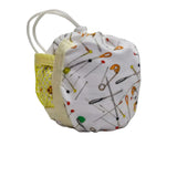 A small fabric pouch with a white background and a print of safety pins in various colors. It features a yellow mesh side pocket with a white zipper and a white elastic loop strap.