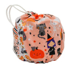 A small fabric drawstring bag with a Halloween print, featuring a peach-pink background with cartoon pumpkins, cats, witches, spiders, and stars, plus a white patterned side panel and white drawstring ties.