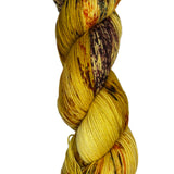Skein of hand dyed fingering weight yarn in the color yellow tan brown red orange speckles