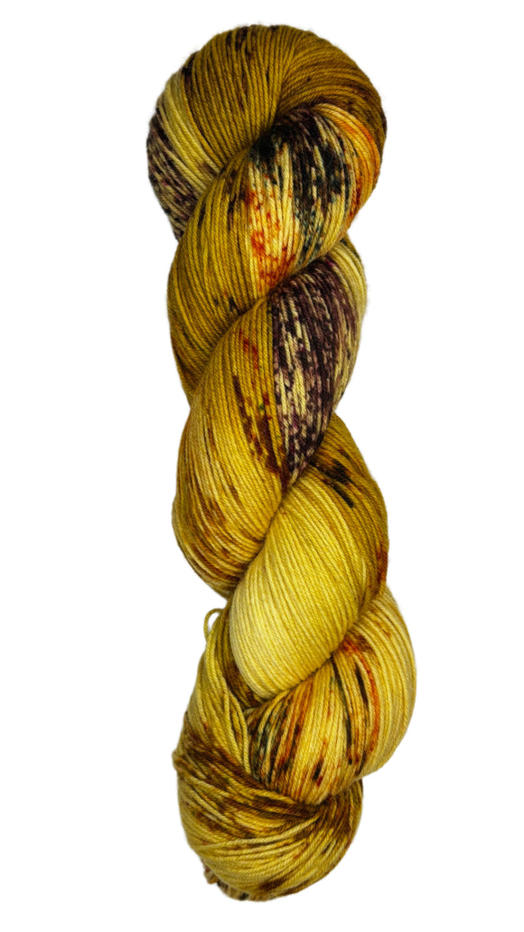 Skein of hand dyed fingering weight yarn in the color yellow tan brown red orange speckles