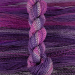Skein of multicolored handspun looking wool yarn in the colors white dark purple light purple pink dark grey