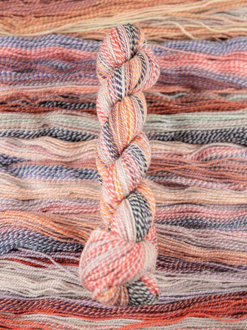 Skein of multicolored handspun looking wool yarn in the colors off-white black orange pink grey