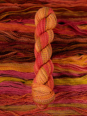 Skein of multicolored handspun looking wool yarn in the colors red pink yellow orange brown