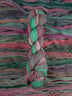 Skein of multicolored handspun looking wool yarn in the colors green pink grey teal brown