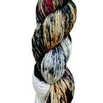 A skein of hand-dyed fingering/sock yarn color tan white blue red black speckles