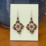 Pair of earrings on a display card with a blue vase in the background