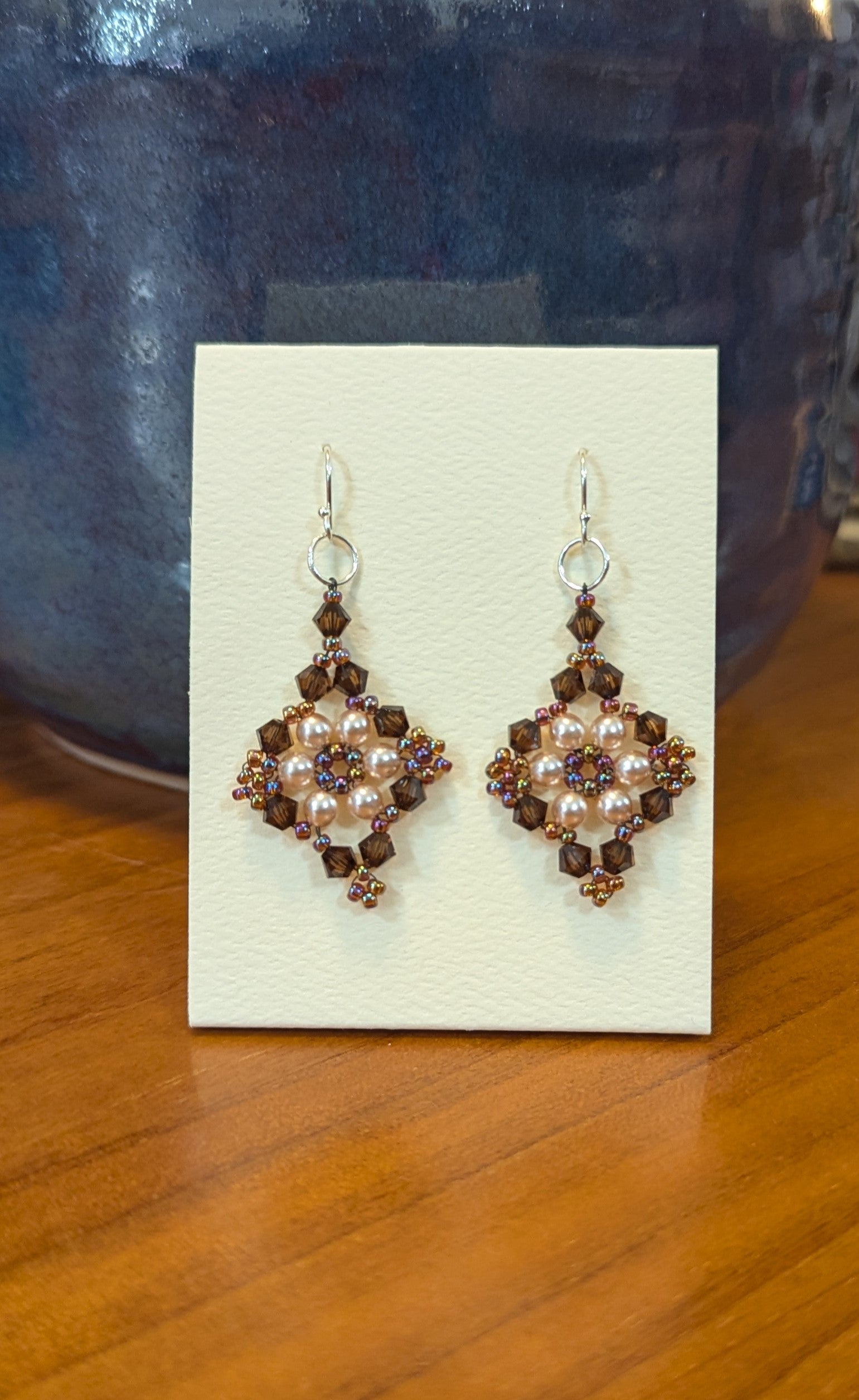 Pair of earrings on a display card with a blue vase in the background