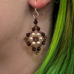 Close-up of an earring with pearls and crystals worn by a person with green hair.