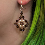 Close-up of an earring with pearls and crystals worn by a person with green hair.