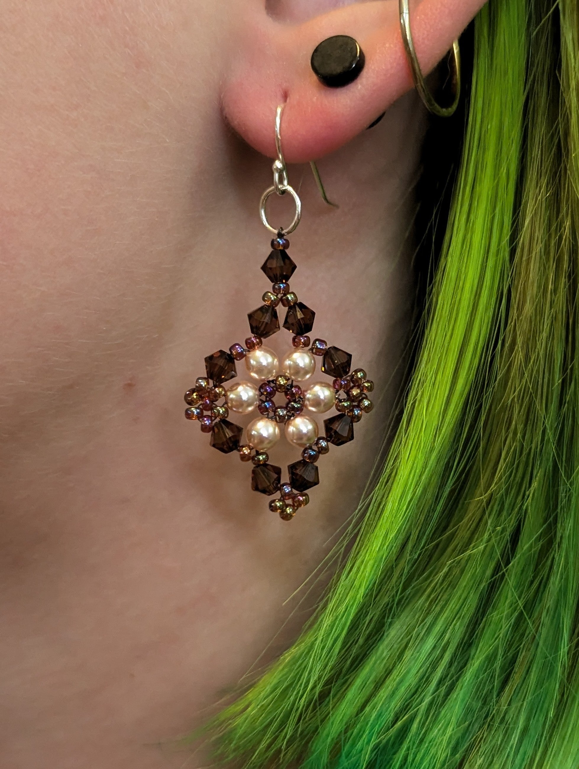 Close-up of an earring with pearls and crystals worn by a person with green hair.