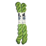 Two mini skeins of green yarn in the color green on a white background