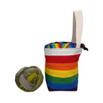 Colorful striped pouch with a handle next to a ball of yarn on a white surface.