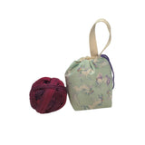 Ball of yarn next to a small fabric bag with a unicorn pattern on a white surface.