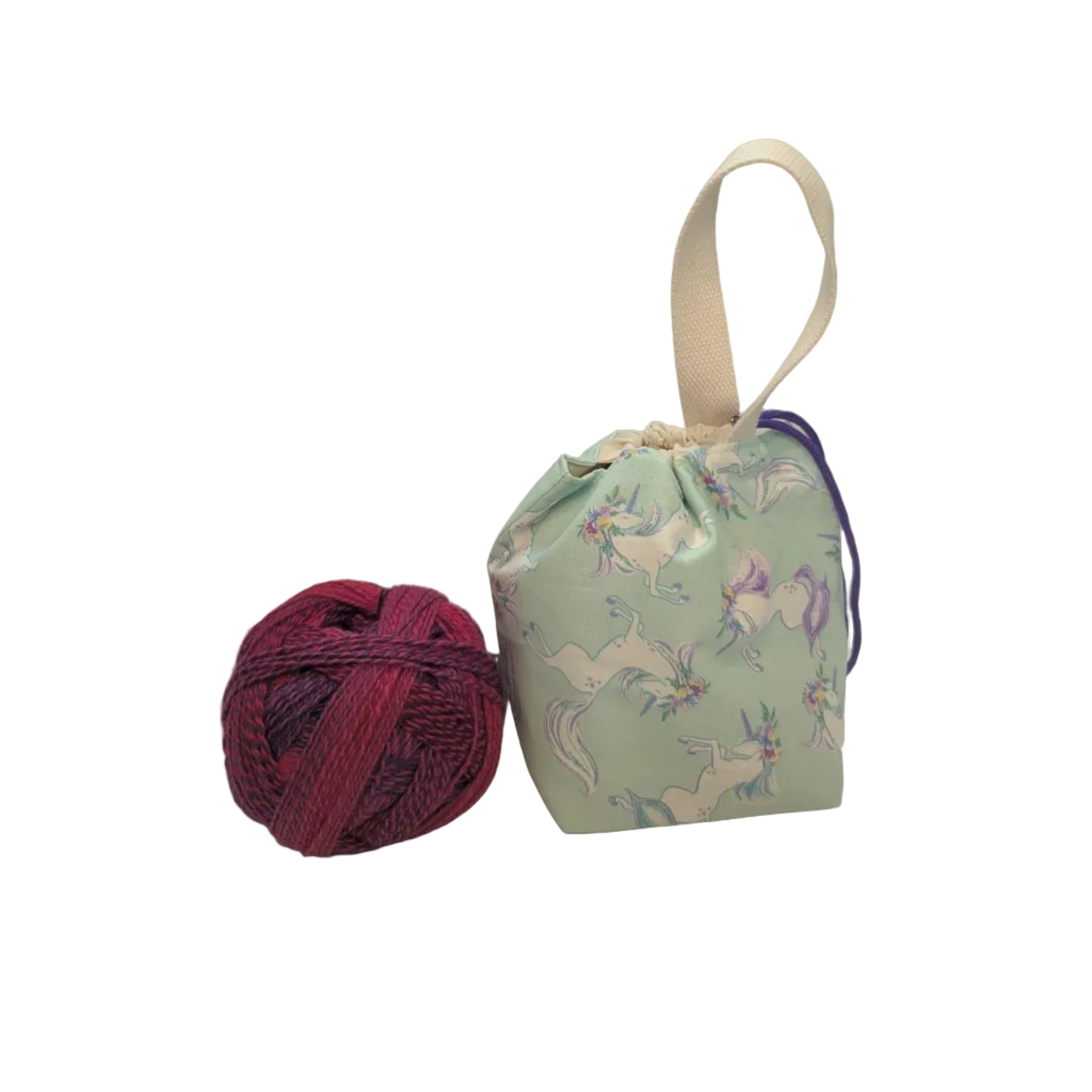 Ball of yarn next to a small fabric bag with a unicorn pattern on a white surface.