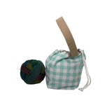A small teal and white gingham drawstring bag with a beige woven handle sits on a white surface next to a ball of multicolored yarn.