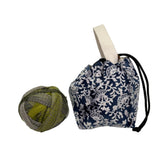 Yarn ball next to a blue and white floral patterned drawstring bag on a white background