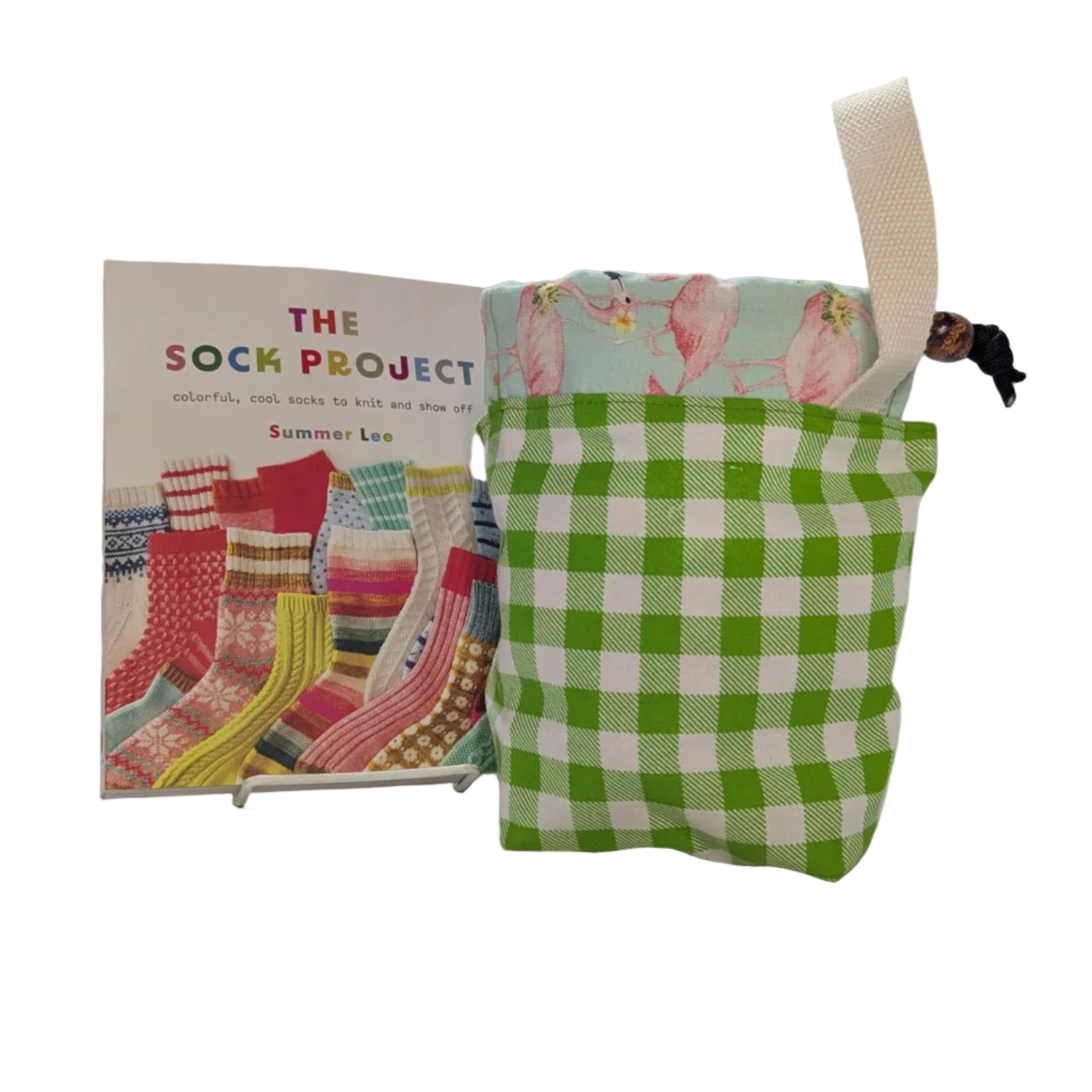 Green checkered pouch with pink flamingo design on a white surface, next to a book titled 'The Sock Project'.