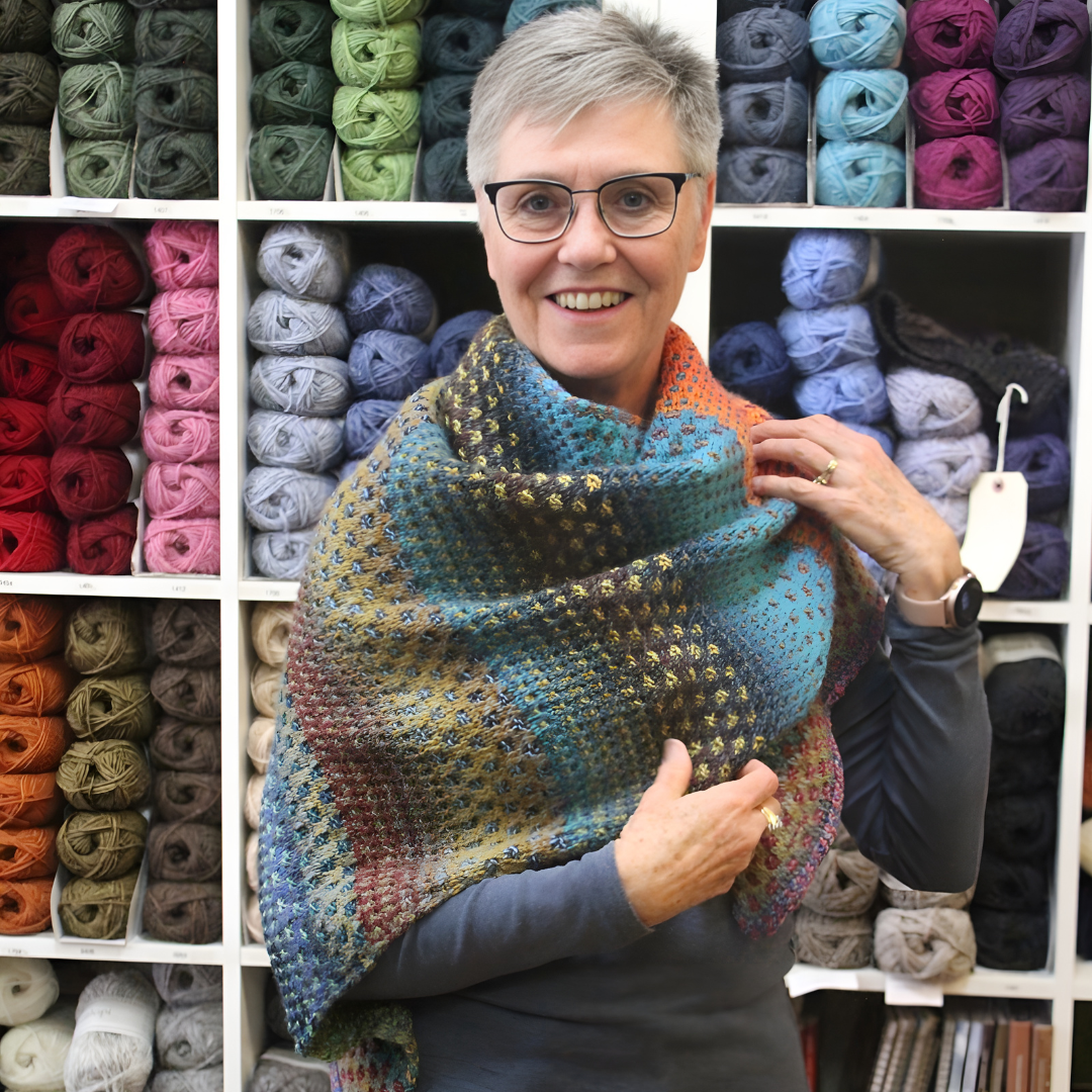 Robbie, Cowgirl Yarn's expert knitting instructor showing off her latest jewel toned shawl with blues and greens and oranges and reds.