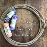 Several skeins of Coastal Cotton Coral Reef yarn in various colors are displayed on a wooden surface, with a rope in the background. The yarn is marked with branding and the text 'Coral Reef' along with 'Aran 185 Yards.
