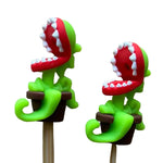 Two green and red stitch stoppers shaped like venus fly traps in plant pots with their mouths open