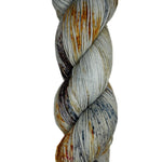 Skein of hand dyed fingering weight yarn in the color grey orange black speckles